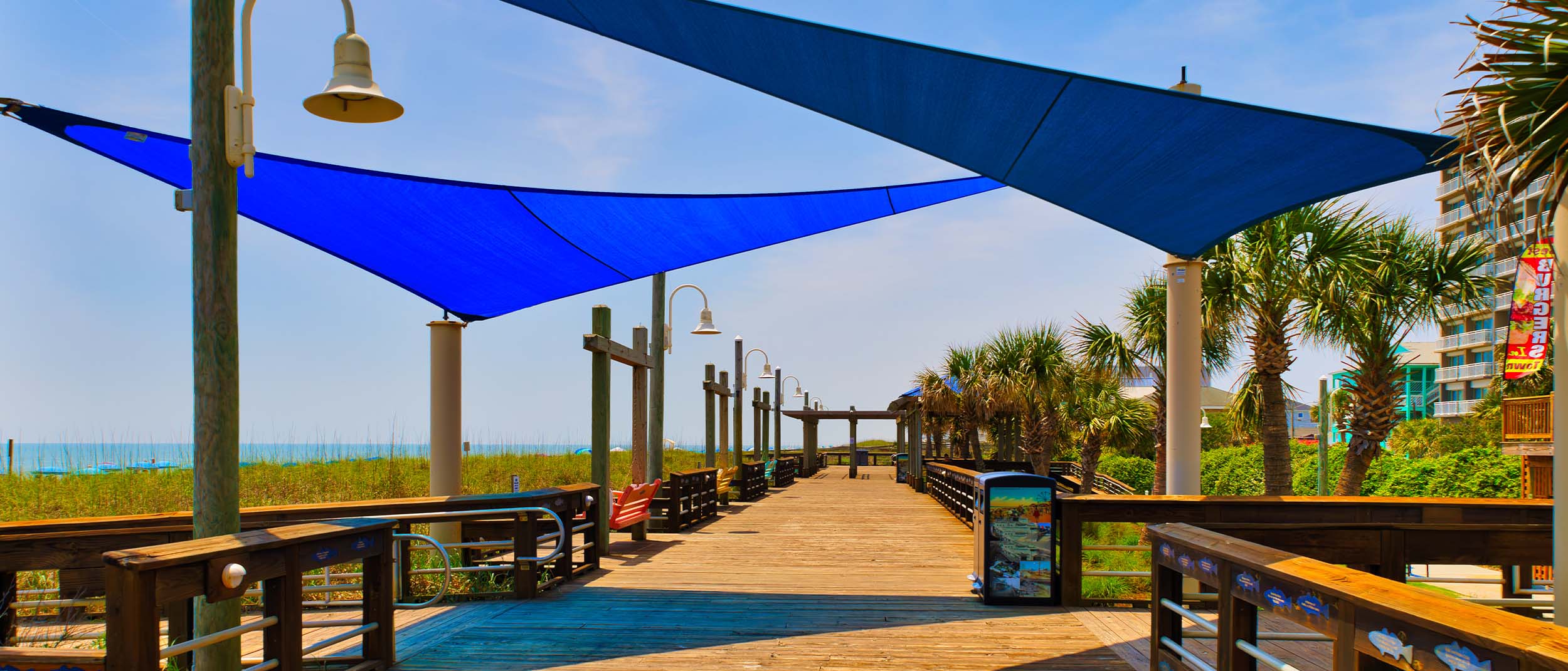 A view down a wooden beach boardwalk with shade tarps and their shadows at Carolina Beach, North Carolina