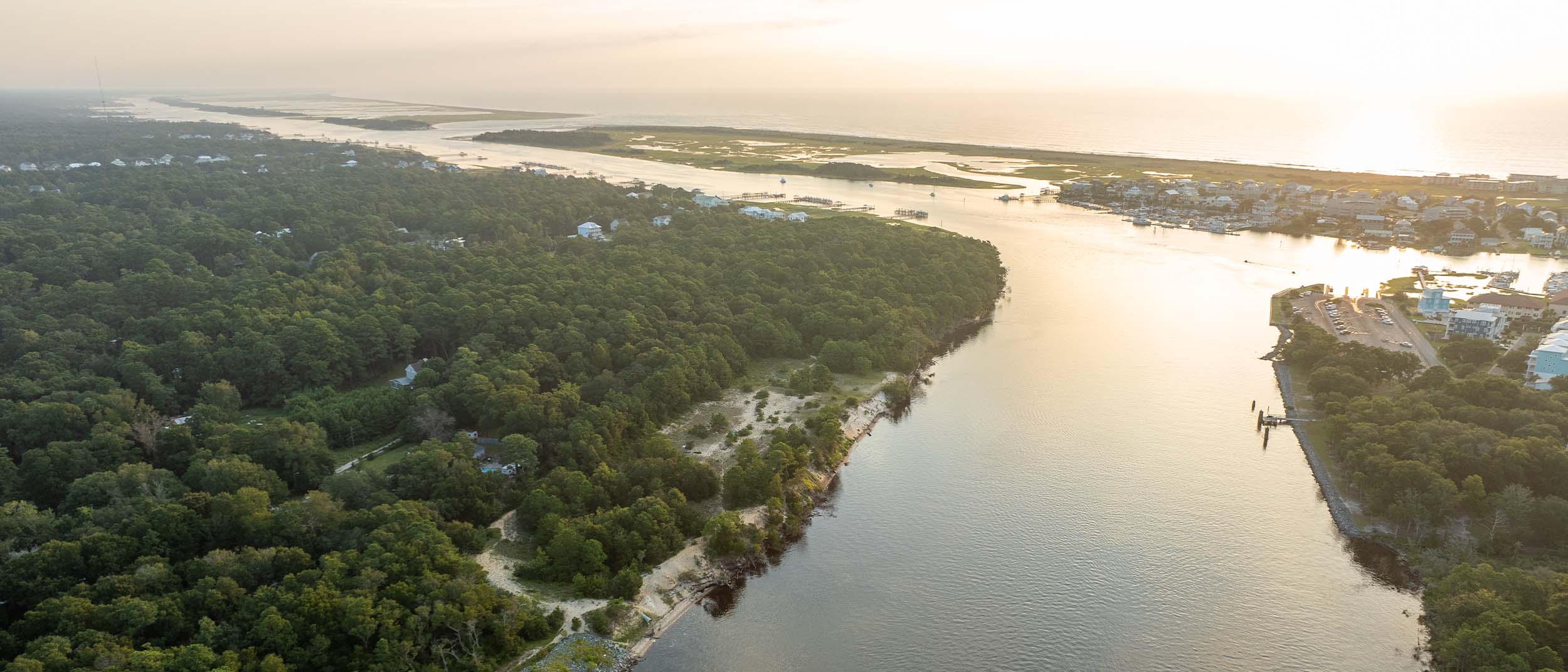 Aerial view of Snow's Cut waterway leading to the Atlantic Ocean, bordered by dense forests and a nearby road, with a boat visible in the water.